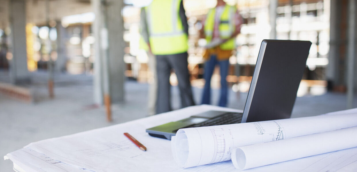 Bauarbeiter auf der Baustelle hinter Werkzeugen und Laptop – Planung und Koordination durch Generalübernehmer in Rosenheim.